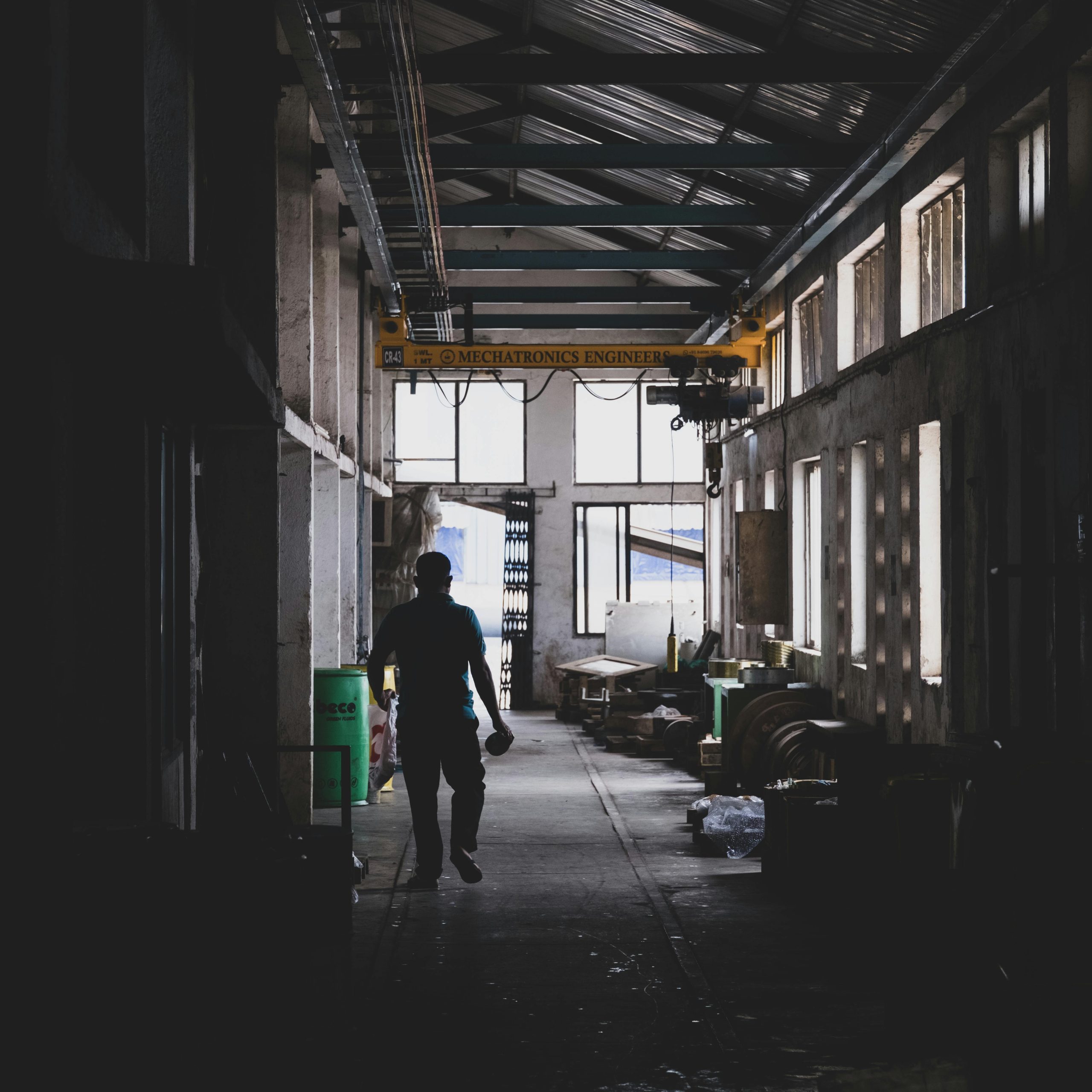 Silhouette of a person walking in a dimly lit industrial warehouse corridor.